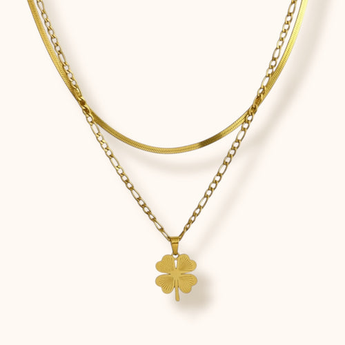 Close-up of layered gold chain necklace with clover pendant