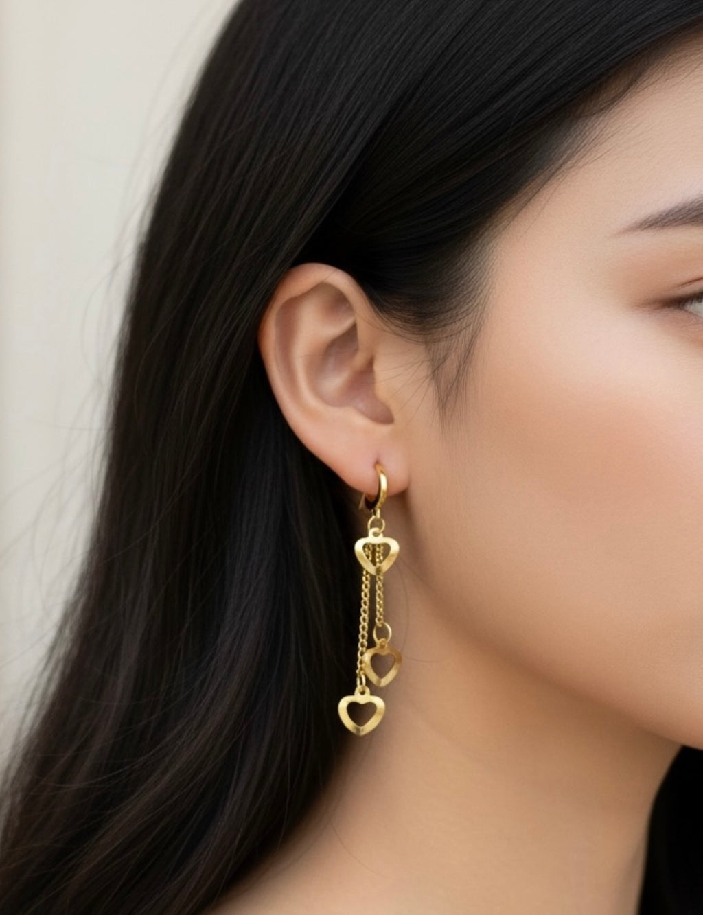 Gold earrings with heart and key charms worn by a person with dark hair.