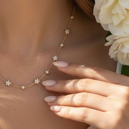 Necklace with star-shaped pendants worn by a person with white roses in the background
